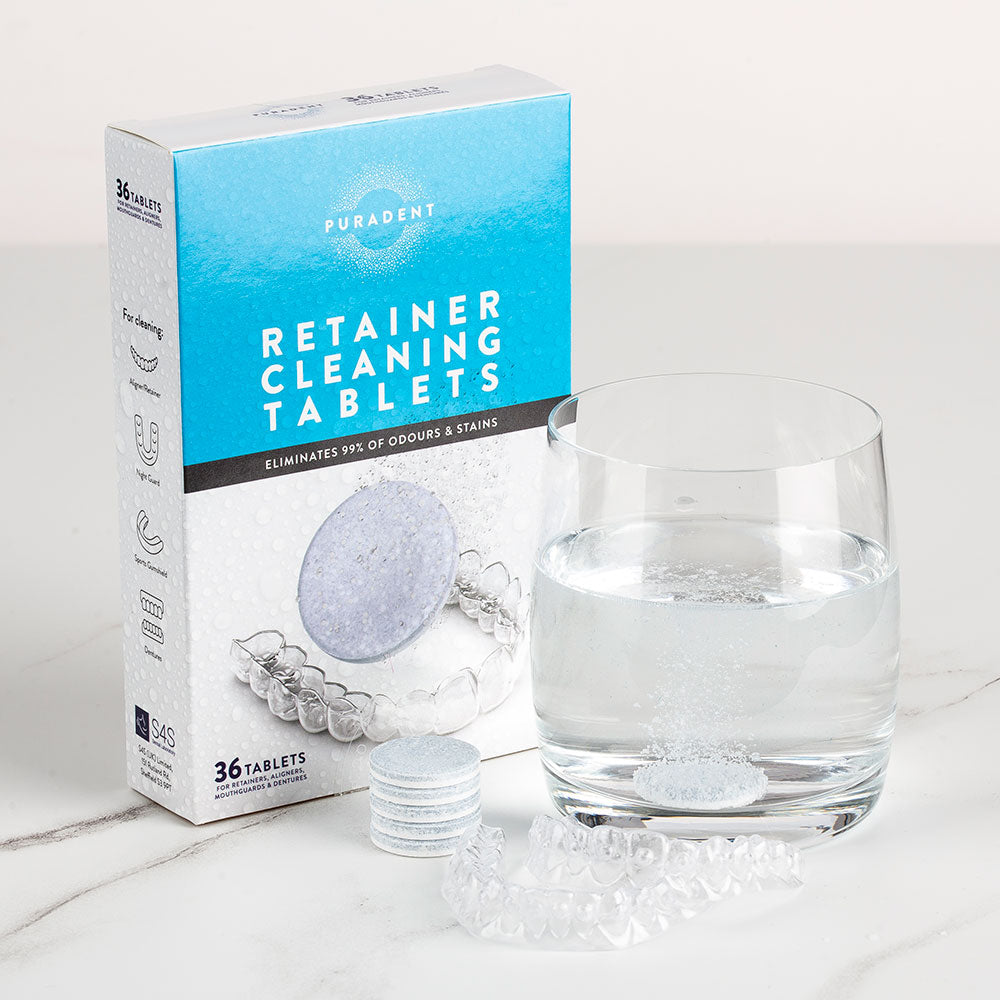 Box of Puradent retainer cleaning tablets with a glass of water and tablet on a white surface